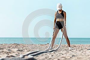 Sporty young woman, Man doing fitness workout on the beach on a sunny day, using two fighting ropes on the beach
