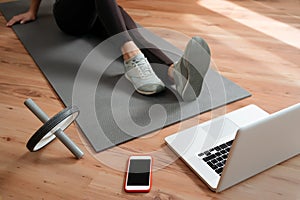 Sporty young woman sitting on exercise mat and watching online workout classes