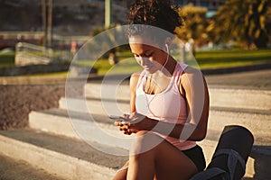 Sporty young woman sitting on park steps using her cellphone