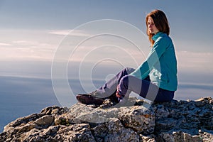 Sporty young woman sitting in a rocky top of the mountain against the blue of sky and sea