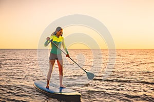 Attractive young woman at stand up paddle board with sunset colors