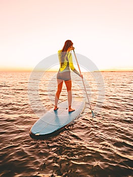 Sporty young woman at stand up paddle board with bright sunset colors