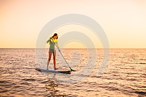 Sporty young woman stand up paddle surfing with beautiful sunset or sunrise colors