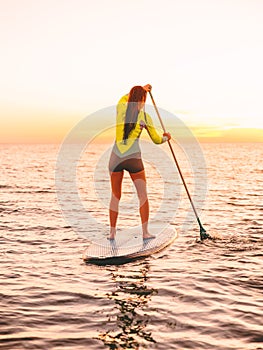 Sporty young woman stand up paddle surfing with beautiful sunset or sunrise colors