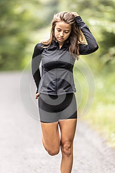 Sporty young woman stretches her leg holding feet behind her by a hand