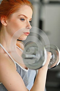 Sporty young woman training with dumbbells in gym