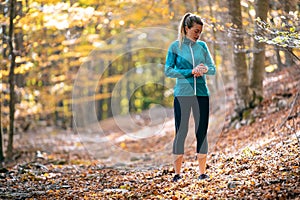 Sporty young woman using her smartwatch before running in the park in the autumn morning