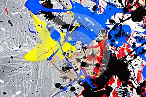 A spot of white and black and yellow and green and red and blue spilled paint on a concrete textured surface