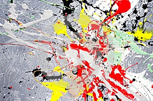 A spot of white and black and yellow and green and red spilled paint on a concrete textured surface