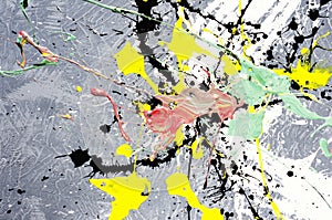 A spot of white and black and yellow and green and red spilled paint on a concrete textured surface