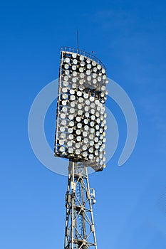Spotlights in stadium against blue summer sky. High metal lighting tower for sports arena or stadium. Bottom up view.