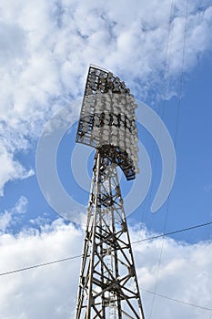 Spotlights in the stadium against the blue summer sky. Stadium lighting tower with searchlights with sky background with clouds.