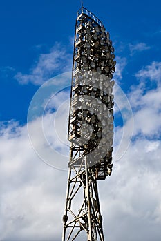 Spotlights in the stadium against the blue summer sky. Stadium lighting tower with searchlights with sky background with clouds.