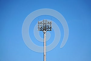 Spotlights tower with a metal pole for the sports arena. Installed around football stadium. Blue sky background.