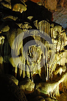 Spotlit stalactites in a cave forming grotesque shapes.