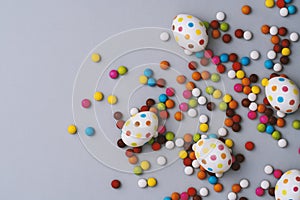 Spotty painted colorful easter eggs and colorful chocolate beans on grey background