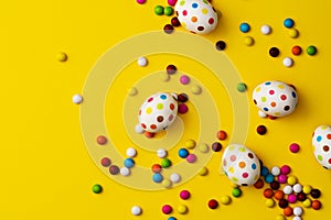 Spotty painted colorful easter eggs and colourful chocolate beans on yellow background