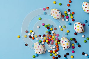 Spotty painted easter eggs and colorful chocolate beans on blue background