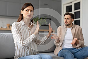 Spouses in heated argument at home, sitting on sofa