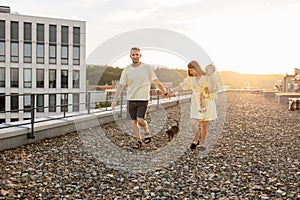 Spouses playing with daughter and dog on building terrace.