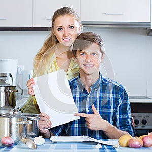 Spouses signing documents and smiling at kitchen