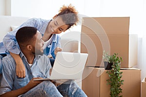 Spouses Using Laptop Computer Sitting On Sofa In New House