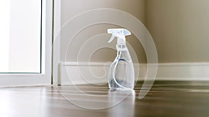 Spray bottle in a side view with a clear liquid inside on the wooden floor in an empty space at home. Spray bottle mockup