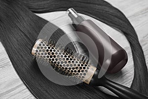 Spray bottle with thermal protection, lock of brunette hair and hairbrush on white wooden table, closeup