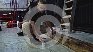 Spray painting of wooden beam in a concert hall. Media. Young man decorating wooden beam by black paint.