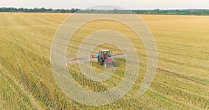 Spraying a field with wheat view from a drone. A tractor sprays wheat with herbicides. The tractor sprays the wheat