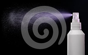 Spraying product in spray bottle over black background.