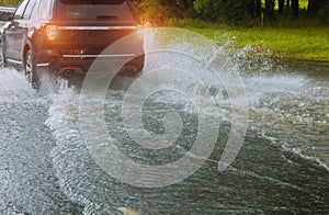 Spraying water of a car moving driving car on flooded road during flood caused by torrential rains. Cars float on water, flooding