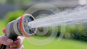 Spraying water with garden hose and adjustable nozzle in slow motion. Man\'s hand holding spray gun watering plants