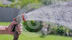 Spraying water with garden hose and adjustable nozzle in slow motion. Man\'s hand holding spray gun watering plants grass in