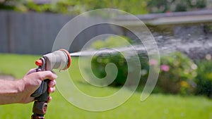 Spraying water with garden hose and adjustable nozzle in slow motion. Man\'s hand holding spray gun watering plants grass in