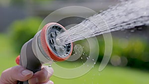 Spraying water with garden hose and adjustable nozzle in slow motion. Man\'s hand holding spray gun watering plants grass in