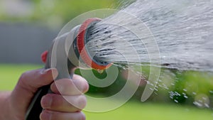 Spraying water with garden hose and adjustable nozzle in slow motion. Man\'s hand holding spray gun watering plants, grass