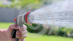 Spraying water with garden hose and adjustable nozzle in slow motion. Man\'s hand holding spray gun watering plants, grass