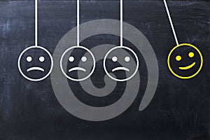 Spread happiness concept with happy and sad faces on newtonâ€™s cradle on blackboard