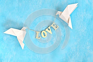 Spread message of love concept. Two white dove origami carrying word LOVE on blue background.