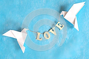 Spread message of love concept. Two white dove origami carrying word LOVE on blue background.