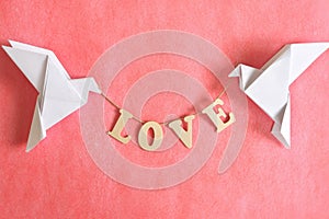 Spread message of love concept. Two white dove origami carrying word LOVE on red background.