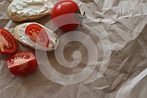 Spreadable bread with curd cheese on a mint paper background with slices of ripe juicy tomato. A whole tomato next to the