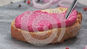Spreading horseradish and beetroot spread with knife on toasted bread