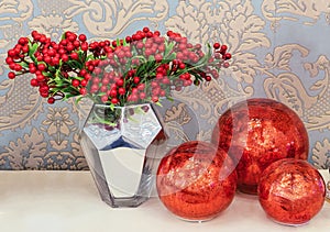 Sprigs of red berries in a mirror vase and three red balls. Composition with viburnum berries