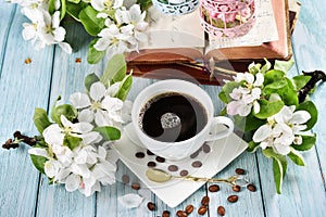 Spring apple blossoms and a cup of black coffee on blue wooden table