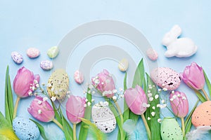 Spring background with flowers, bunny, colorful eggs and feathers on blue table top view. Happy Easter card.