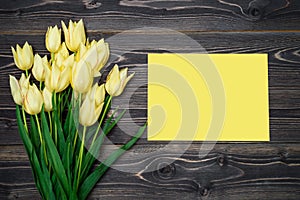 Spring background with yellow tulip flowers and yellow sheet of paper, copy space. Flat lay, top view, horizontal.
