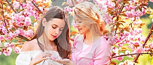 Spring banner with women girlfriends outdoor. Two Beauty spring girls with blooming sakura cherry Flovers.