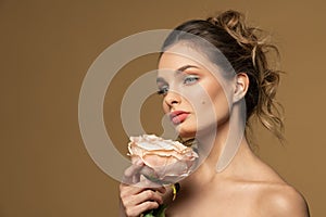 Spring beauty girl with a rose looking away on beige background
